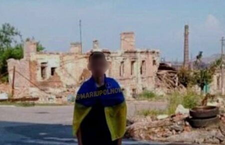 У Маріуполі юнак сфотографувався біля розбомбленого будинку з прапором України